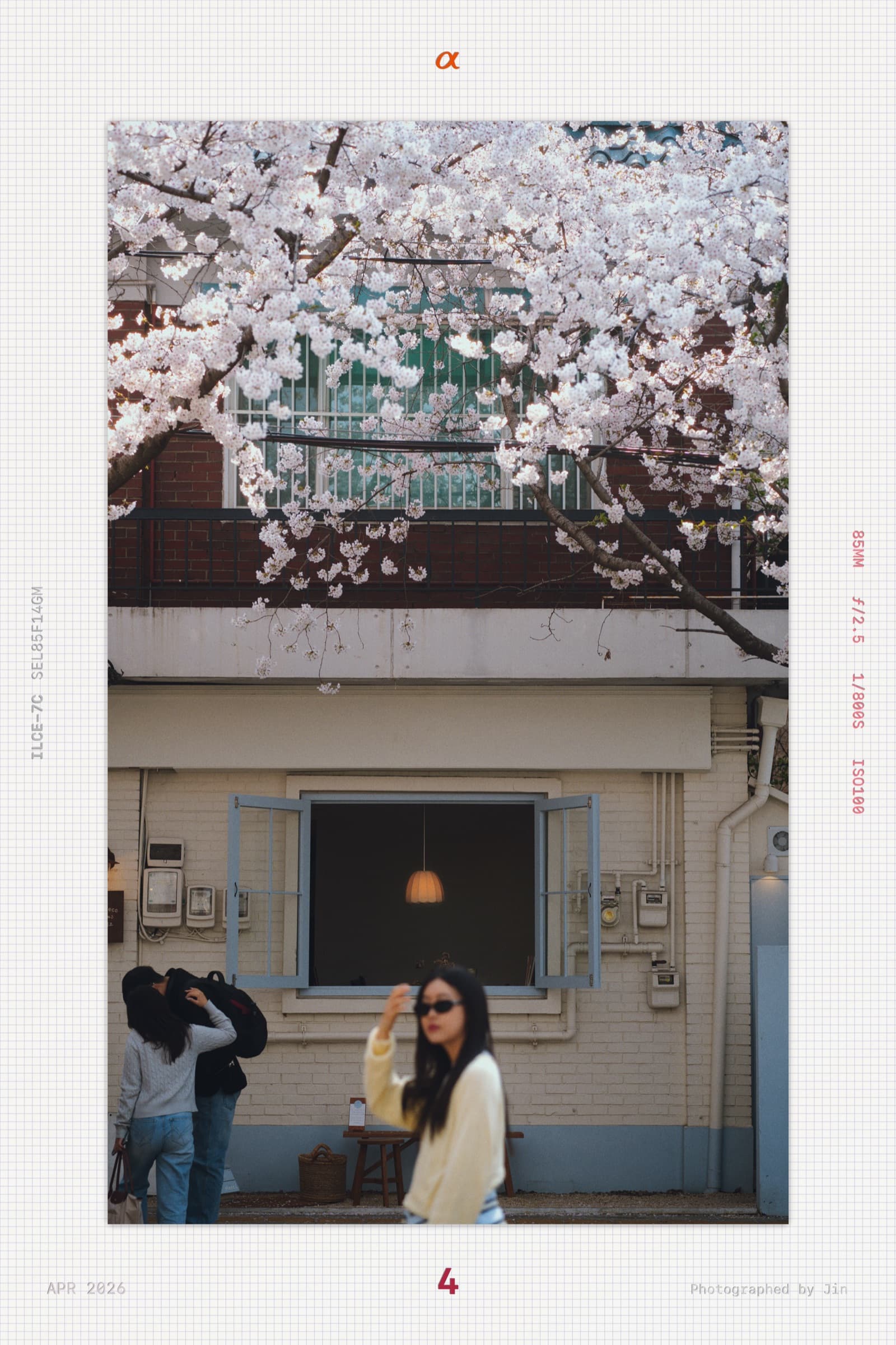 A woman in sunglasses posing in front of a cafe window with cherry blossoms behind her